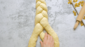 Overhead shot of hands braiding challah dough into a three strand braid.