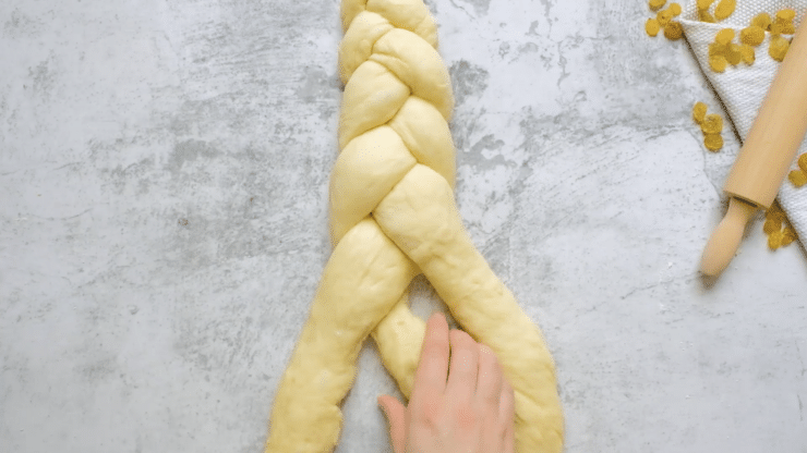 Overhead shot of hands braiding challah dough into a three strand braid.