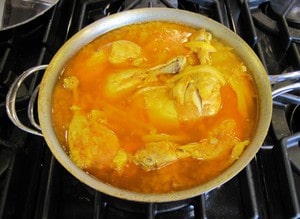 Chicken quarters simmering in stock in a saucepan.
