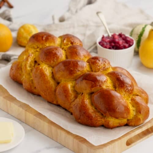 Horizontal image of a loaf of pumpkin challah bread on a wooden cutting board.