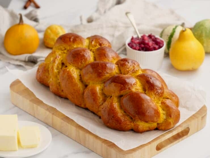Horizontal image of a loaf of pumpkin challah bread on a wooden cutting board.