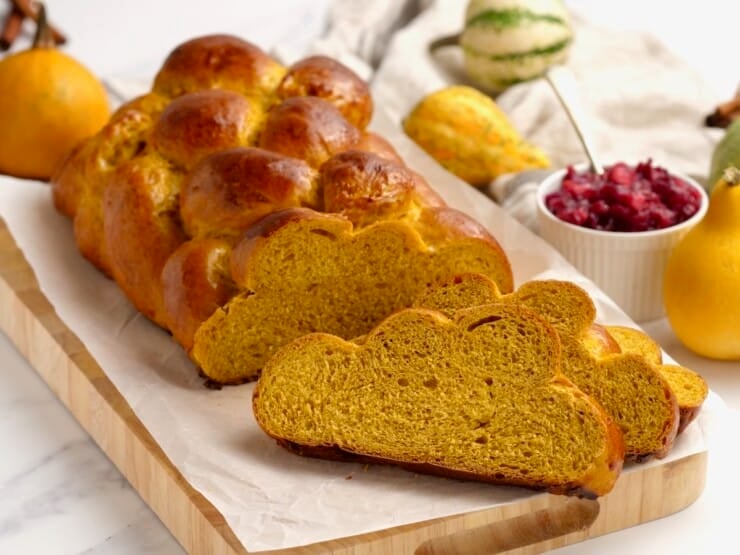 Horizontal image of a braided loaf of pumpkin challah. Two pieces have been sliced off and are sitting next to the loaf.