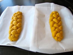 Two braided challah loaves on parchment lined baking sheets.