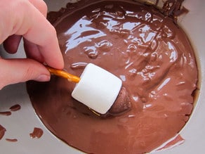 Hand dipping candy dreidel in melted chocolate.