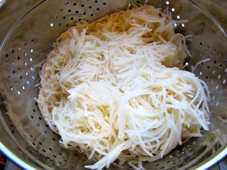 Shredded potatoes in a colander, draining.