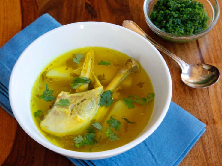 Close-up of Chicken Yemenite soup topped with chopped cilantros served in a white bowl and on blue table cloth with a spoon on the side