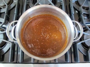 Stirring peanut butter into butter and sugar in a saucepan.