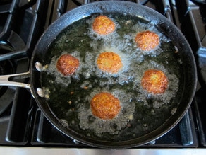 Six falafel balls frying in black frying pan in hot oil.
