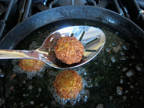 Falafel being removed from frying pan with slotted spoon.