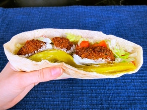 Falafel pita in hand with pickles, lettuce and tomatoes.