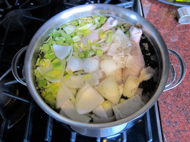 Whole chicken and aromatics in a stockpot of water.