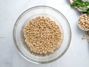 Horizontal image of dried chickpeas (garbanzo beans) soaking in a glass bowl of water.
