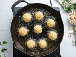 Horizontal overhead image of falafel balls frying in a pan.