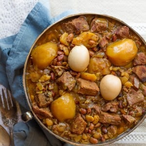 A traditional Jewish stew with beef, eggs, and potatoes on a plate and a fork on the side