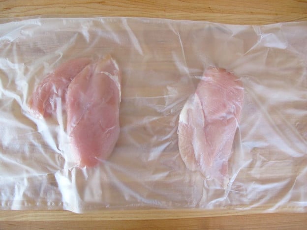 Chicken breasts between layers of plastic wrap.