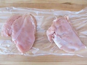 Chicken breast pounded flat in layers of plastic wrap.