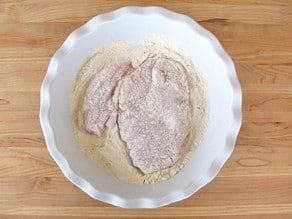 Dredging chicken breast in matzo meal.