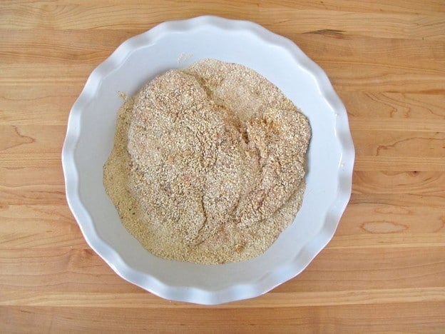 Dredging chicken breast in matzo meal.