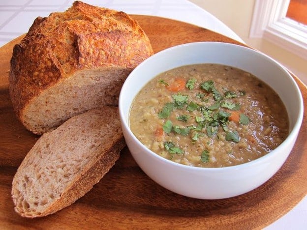 An image of a Lentil stew in a white bowl paired with a slice of crusty bread on the side.