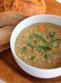 A bowl of lentil soup paired with a bread on a wooden plate