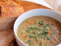 An image of a Lentil stew in a white bowl paired with a slice of crusty bread on the side.