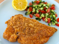 Crispy Passover Chicken Schnitzel on a white plate with lemon wedges and chopped vegetables