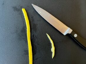 Citrus peel strip with edge trimmed off to make a straight even line, paring knife beside it, in preparation for making a citrus twist.