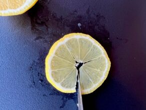 Paring knife cutting notch at the bottom of a citrus lemon round slice.