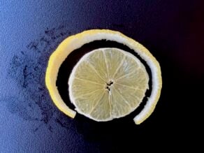 Lemon peel sliced neatly away from lemon round in preparation for making a lemon twist.