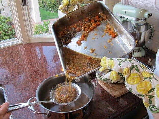 Straining beef pan drippings into a saucepan.