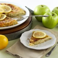 A plate of food with sliced lemons on a pancake and apples on the side