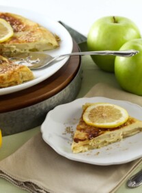 A plate of food with sliced lemons on a pancake and apples on the side