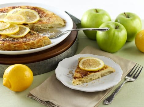 A plate of food with sliced lemons on a pancake and apples on the side