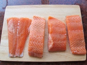 Seasoning salmon fillets on a cutting board.