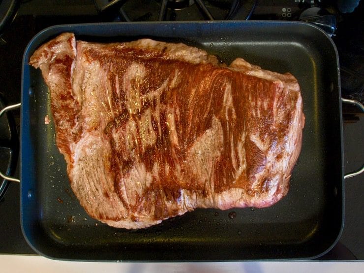 Browned brisket in roasting pan on stovetop.