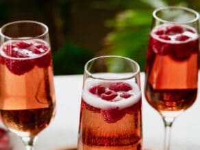 Horizontal angled close up shot of a bright pink kir royale drink in three champagne flutes.