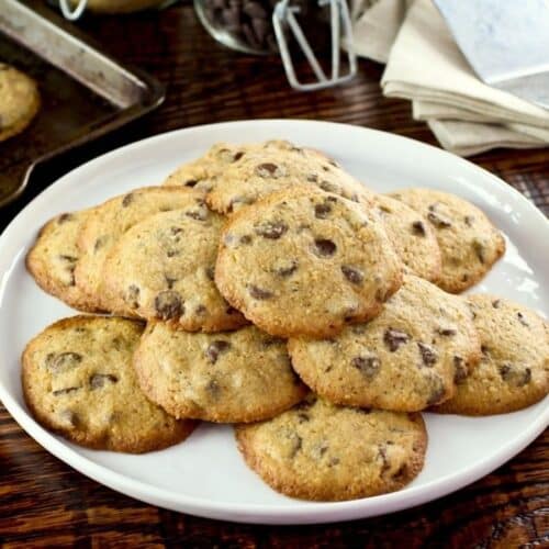 Passover matzo chocolate chip cookies on white plate on wooden background with napkins and baking tray in background.