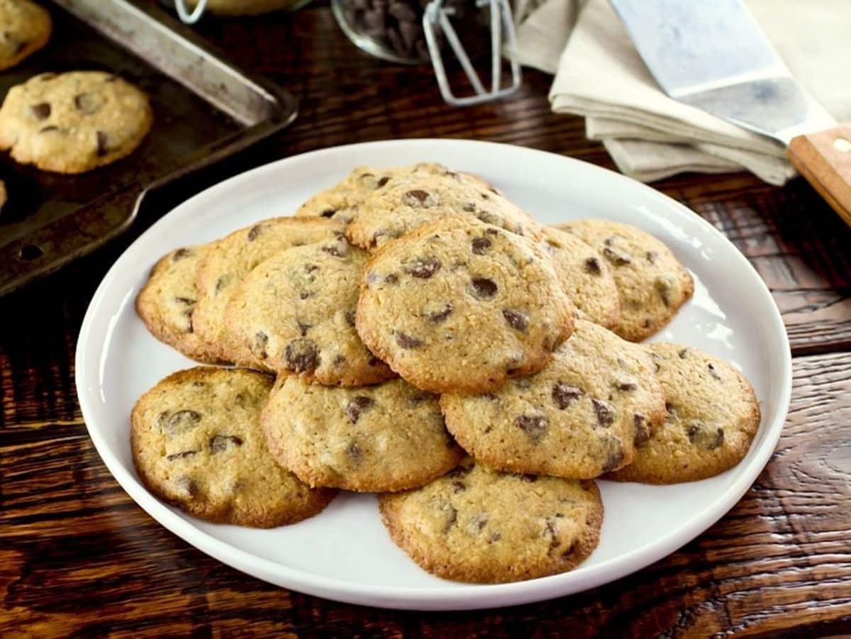 Passover matzo chocolate chip cookies on white plate on wooden background with napkins and baking tray in background.