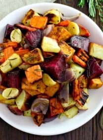 Overhead shot of oven roasted root vegetables with beets, carrots, potatoes, and parsnip. Spoon and fresh herbs on the side, cloth napkin above.
