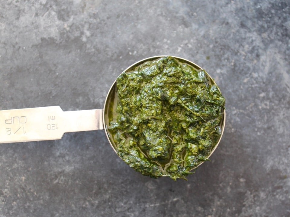 Close up of a measuring cup filled with freshly made basil pesto.