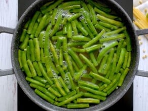 A large pot of green beans simmering in hot water on an induction cooktop.