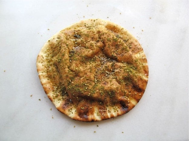 Sprinkling seasoning over oiled pita rounds.
