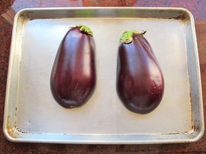 Two fresh eggplant halves on baking sheet.