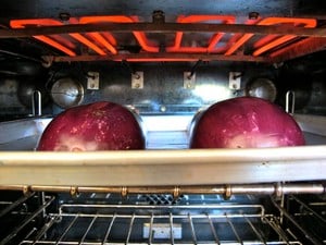 Two eggplant halves on baking sheet under oven broiler.