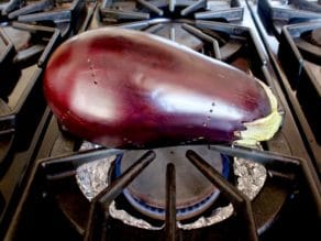 Pierced eggplant on top of foil lined range burner.