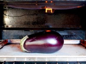 Whole eggplant on baking sheet under broiler.
