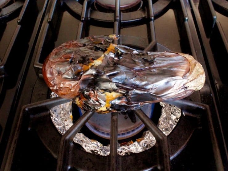 Roasted eggplant on top of foil lined range burner., skin charred.