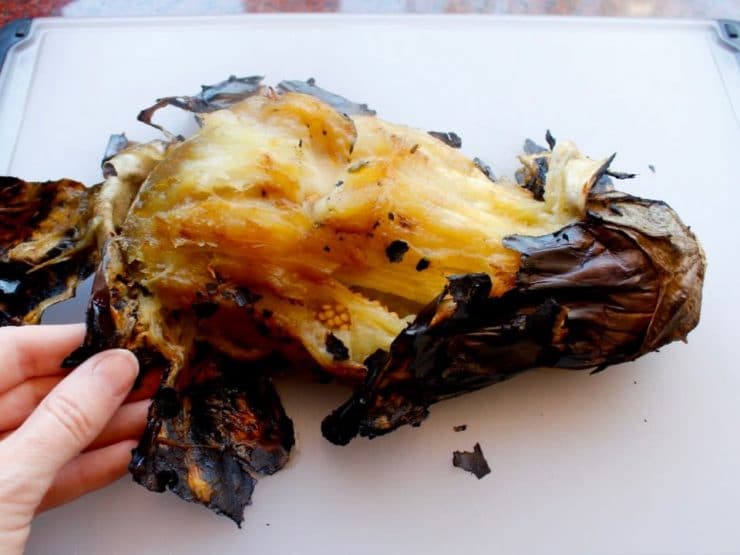Half-peeled charred and roasted eggplant, fingers peeling.