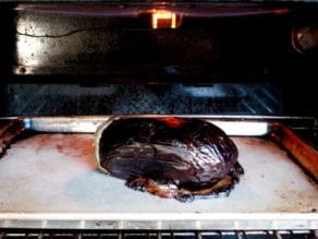 Roasted collapsing eggplant under oven broiler on baking sheet, skin charred.