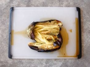 Charred and roasted eggplant sliced open on cutting board.